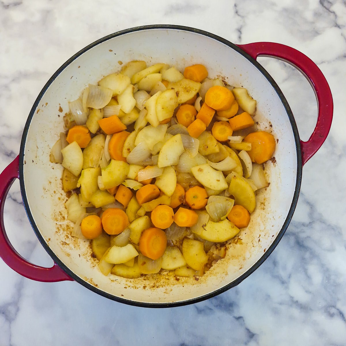 Onions, carrots and apples being sauteed in a casserole dish.