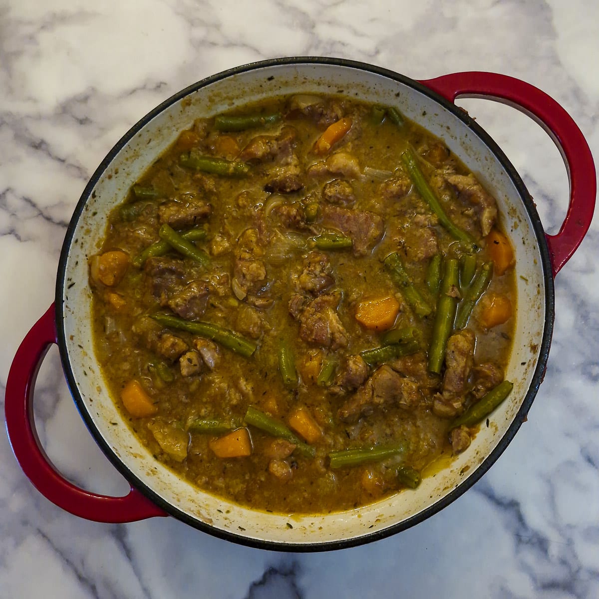 A fully cooked pork and apple casserole in brandy gravy in a casserole dish.