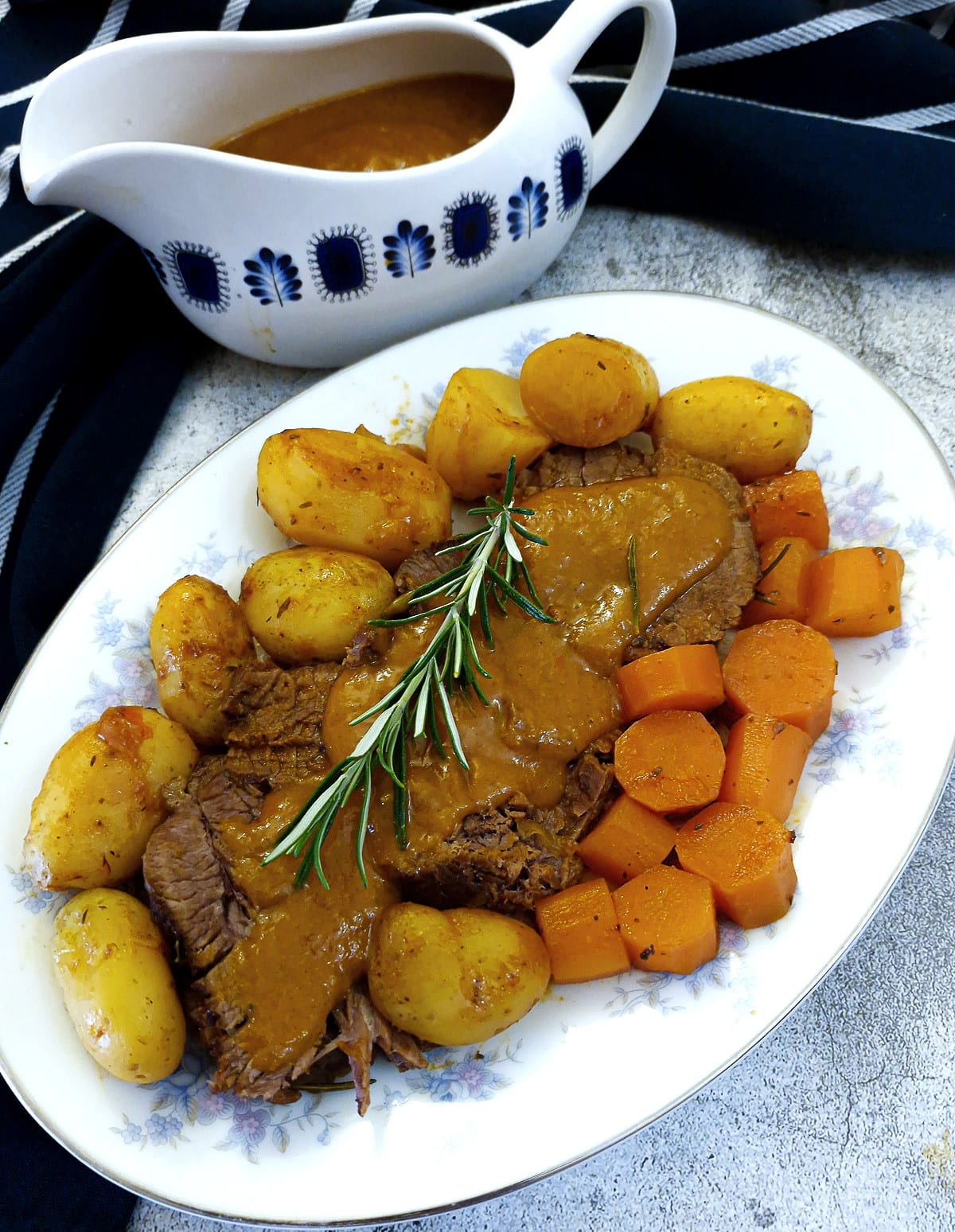 Sliced brisket on a serving platter with potatoes and carrots. Gravy has been poured over the meat.
