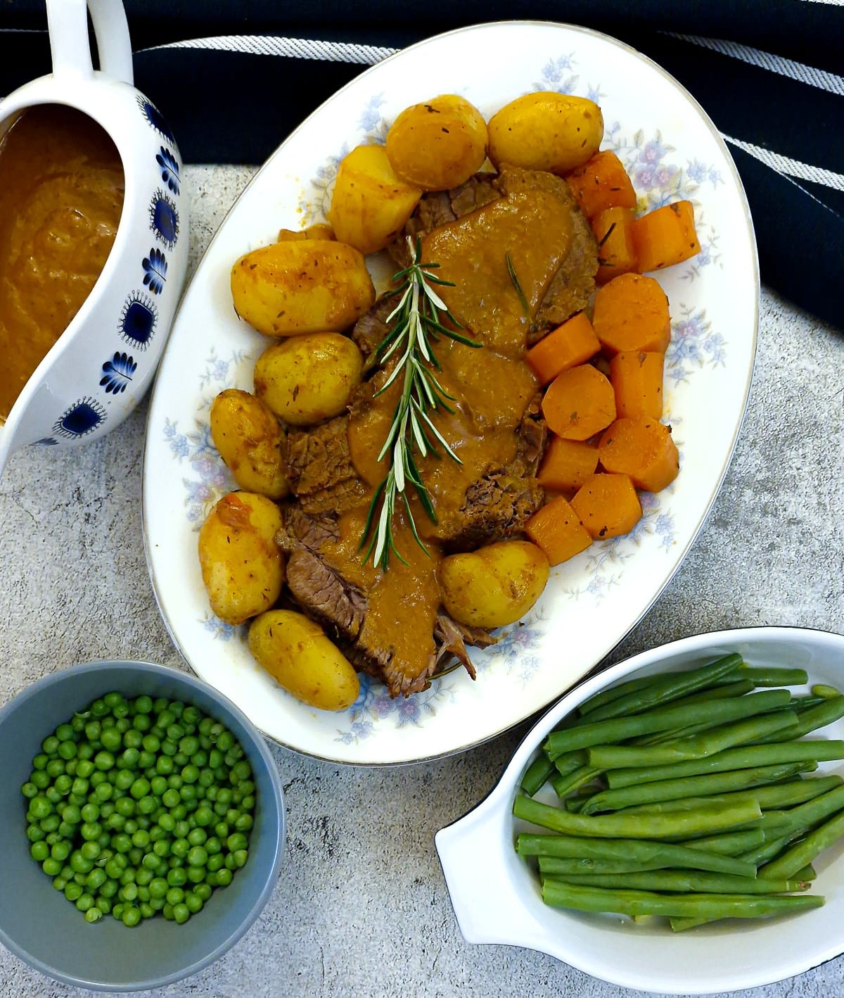 Sliced brisket and vegetables on a plater with dishes of green beans and peas alongside.