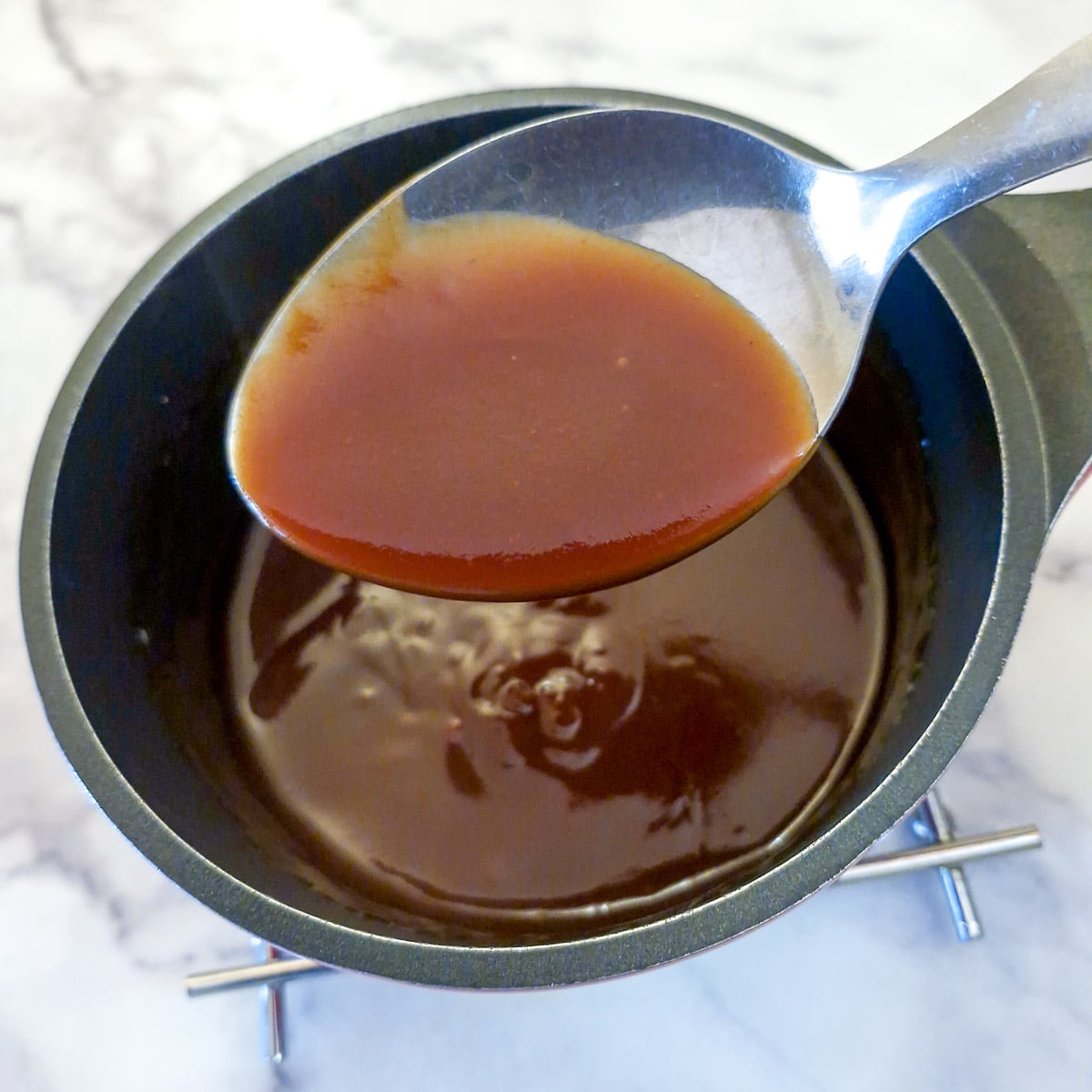 Thickened sweet and sour sauce on a spoon held over the saucepan.