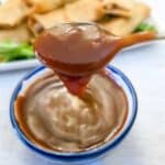 A spoonful of sweet and sour dipping sauce being lifted from a small bowl.