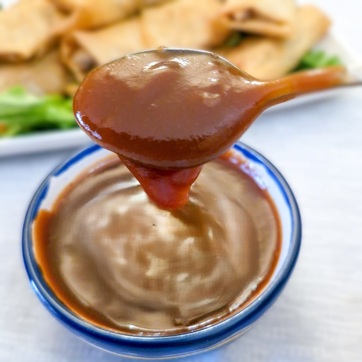 A spoonful of sweet and sour dipping sauce being lifted from a small bowl.