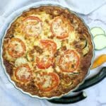 Overhead shot of a baked zucchini quiche with tomato and cheese topping.