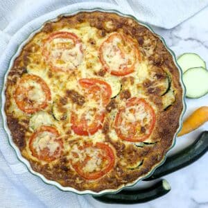 Overhead shot of a baked zucchini quiche with tomato and cheese topping.