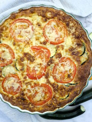 Overhead shot of a baked zucchini quiche with tomato and cheese topping.