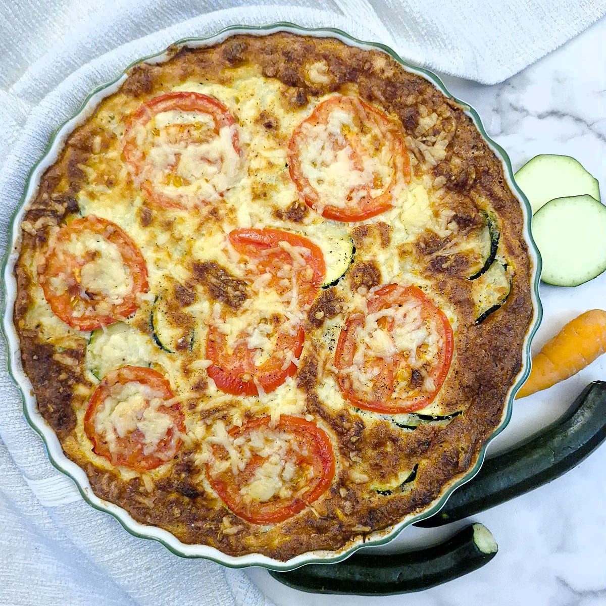 Overhead shot of a baked zucchini quiche with tomato and cheese topping.