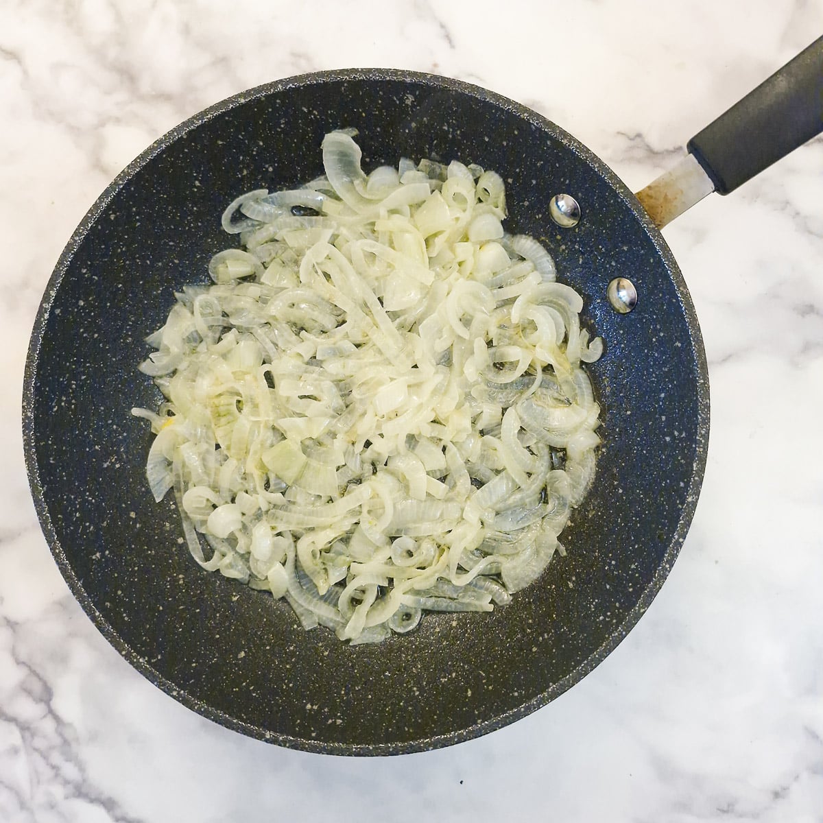 Sliced onions softening in a frying pan.