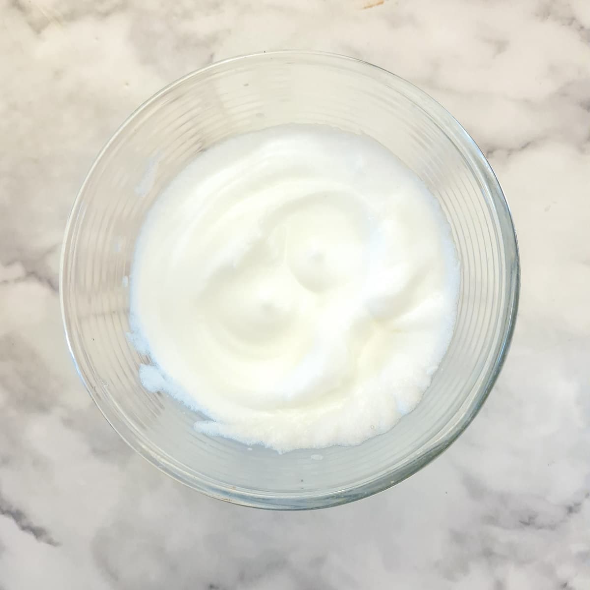 Egg whites whisked to stiff peaks in a glass bowl.