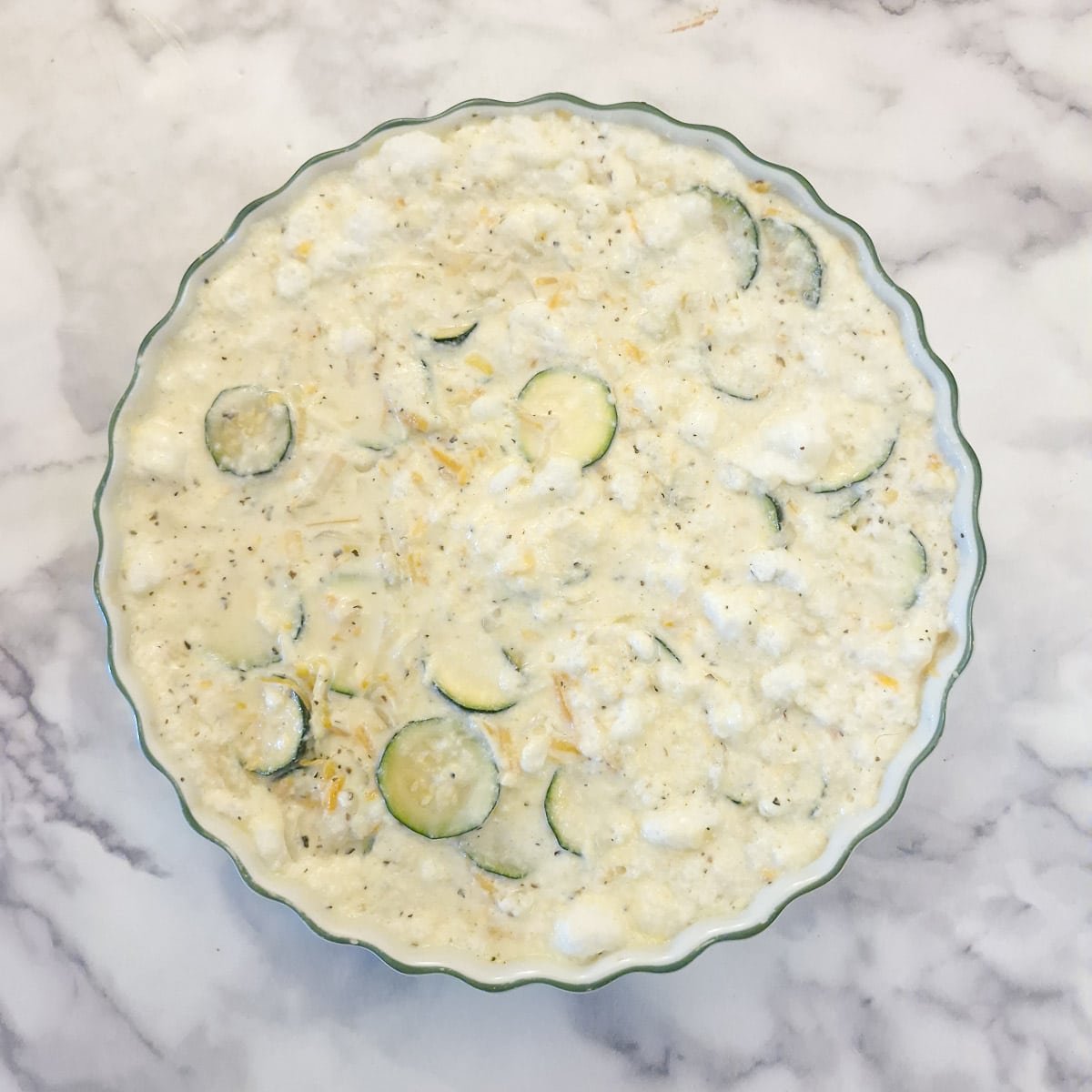 The quiche batter transferred into a 10-inch white baking dish.