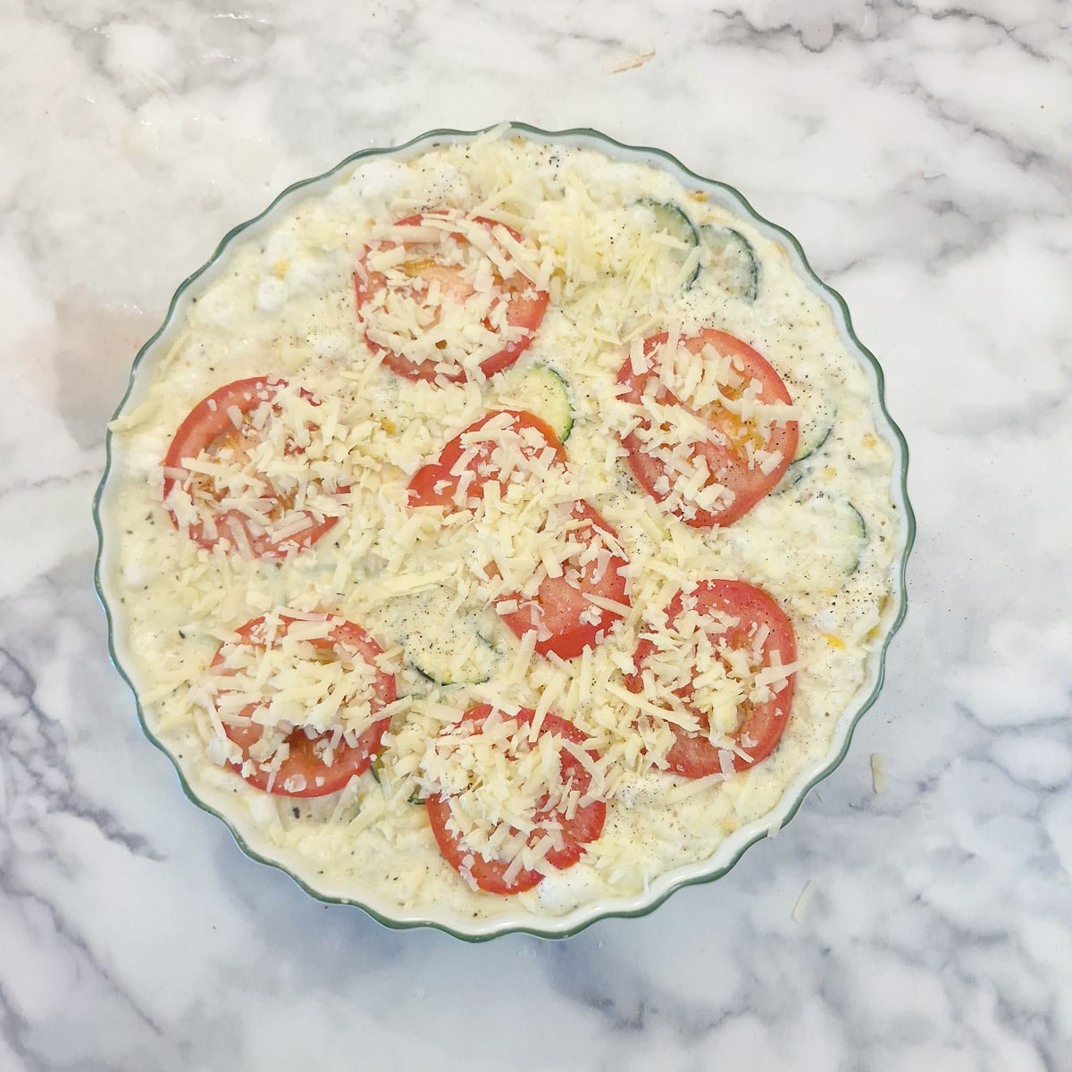 Slice tomatoes covered with grated cheese arranged on top of the quiche.