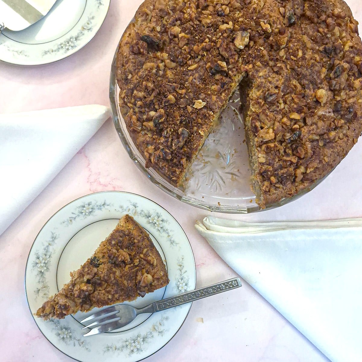 Overhead shot of a slice of apple cake on a plate alongside the whole caike.