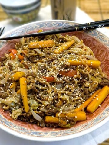 A serving dish filled with easy beef chow mein. There is a pair of chopsticks balanced on the dish.