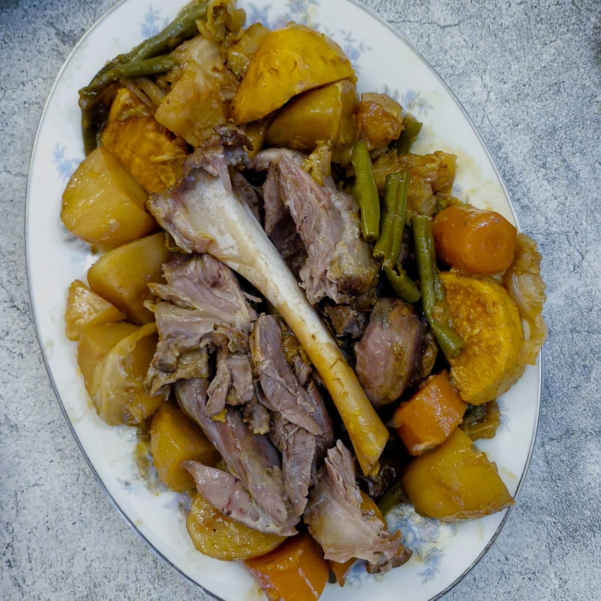 Shredded lamb shank on a serving platter with vegetables. The bone from the shank is resting on top of the meat to show how the meat has falled from the bone.
