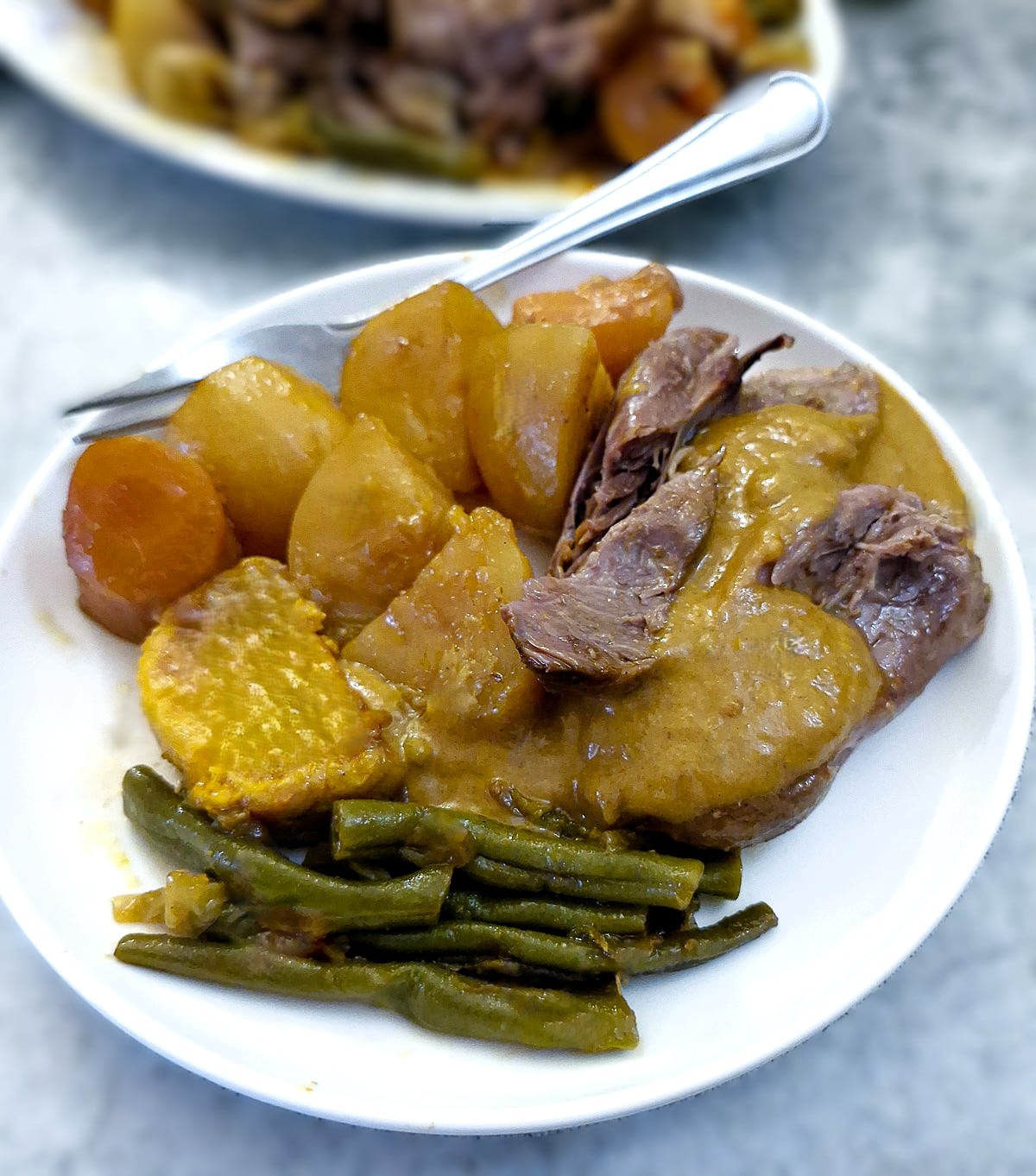 A serving of lamb shank of a plate with vegetables, smothered in thick gravy.