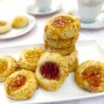 A pile of coconut jam thumbprint cookies on a white plate.