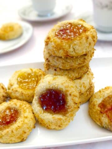 A pile of coconut jam thumbprint cookies on a white plate.