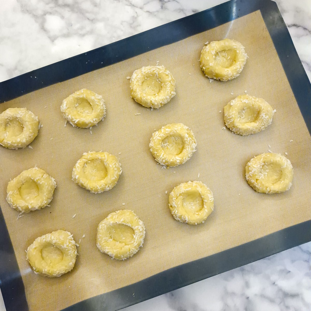 12 balls of dough on a baking tray.  Each ball has had an indentation pressed into it with a teaspoonn.