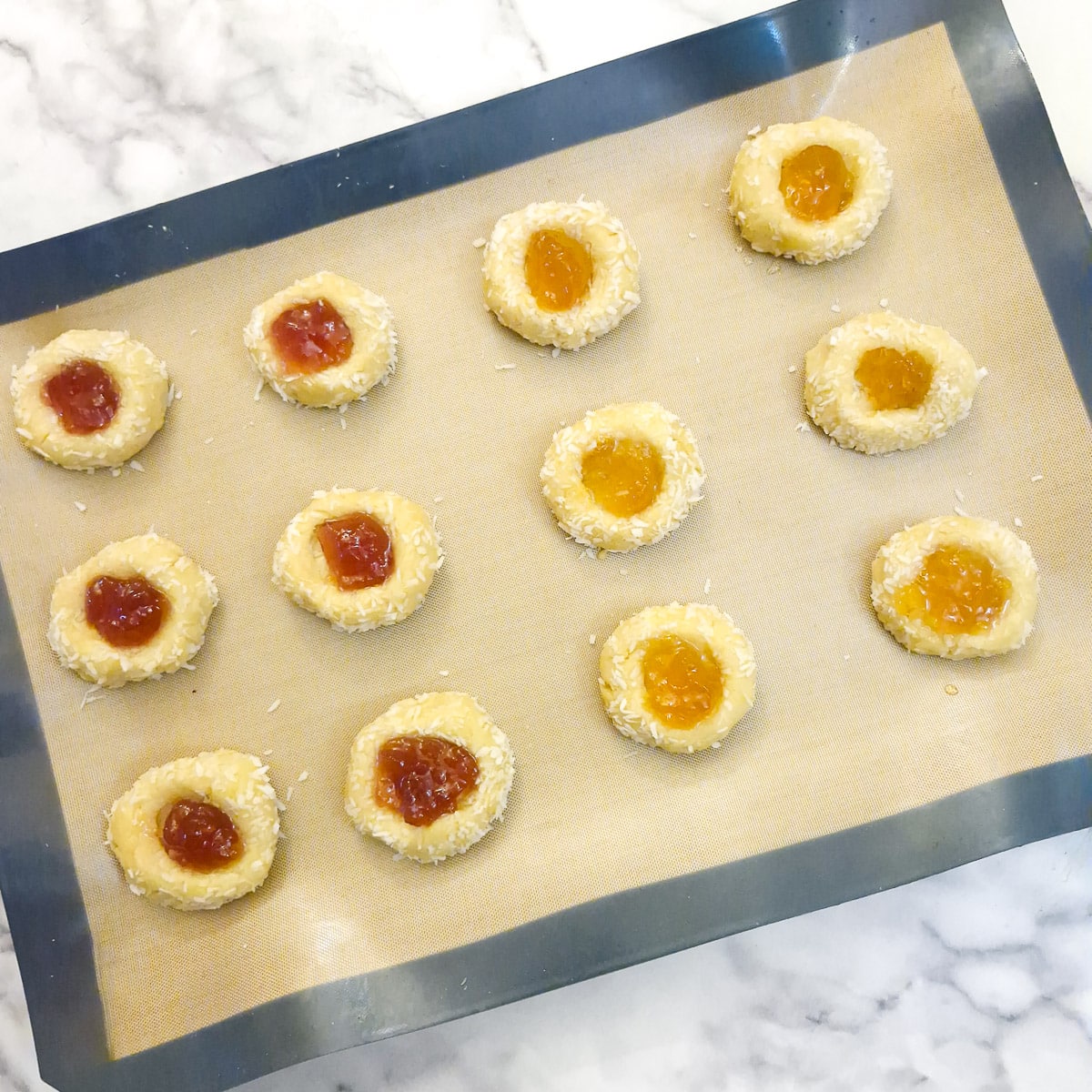 12 raw thumbprint cookies filled with jam, ready to go into the oven.