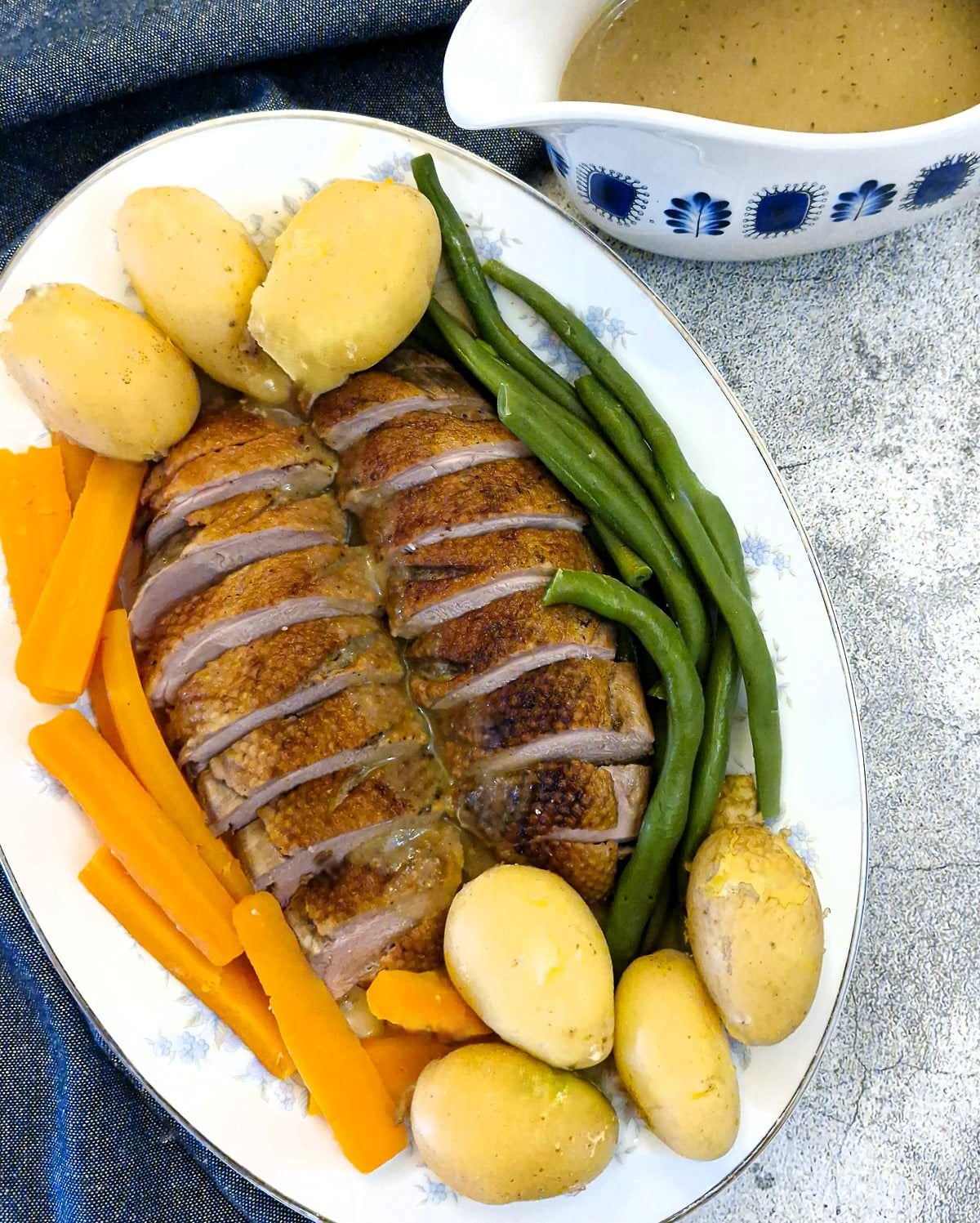 Duck breasts and vegetables on a serving platter with a gravy boat of orange sauce.