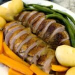 Slices of Duck a l'Orange on a serving platter with carrots. beans and boiled baby potatoes.
