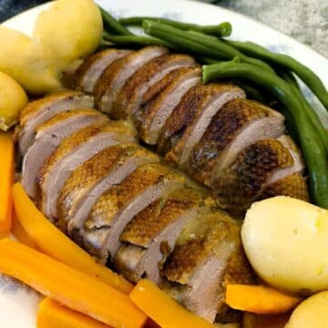 Slices of Duck a l'Orange on a serving platter with carrots. beans and boiled baby potatoes.