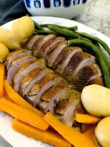 Slices of Duck a l'Orange on a serving platter with carrots. beans and boiled baby potatoes.