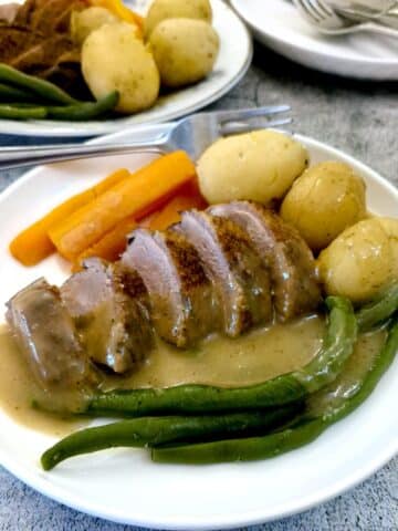 Duck a l'Orange on a dinner plate with vegetables and a helping of gravy.