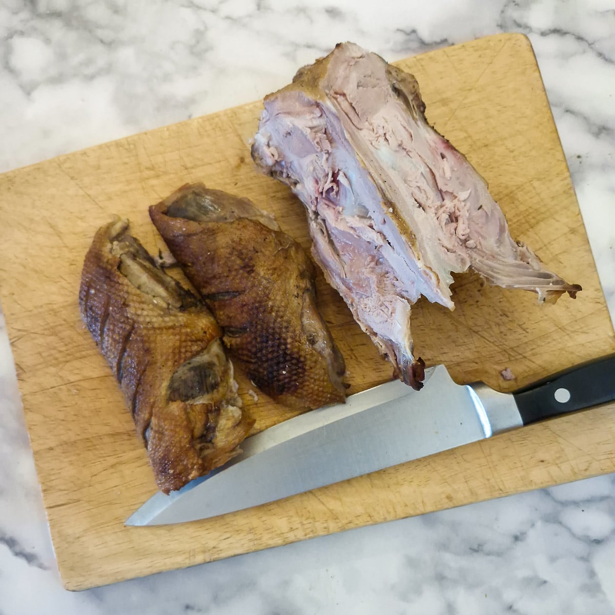Two duck breasts which have been removed from the carcass. The carcass and a sharp knife are alongside..