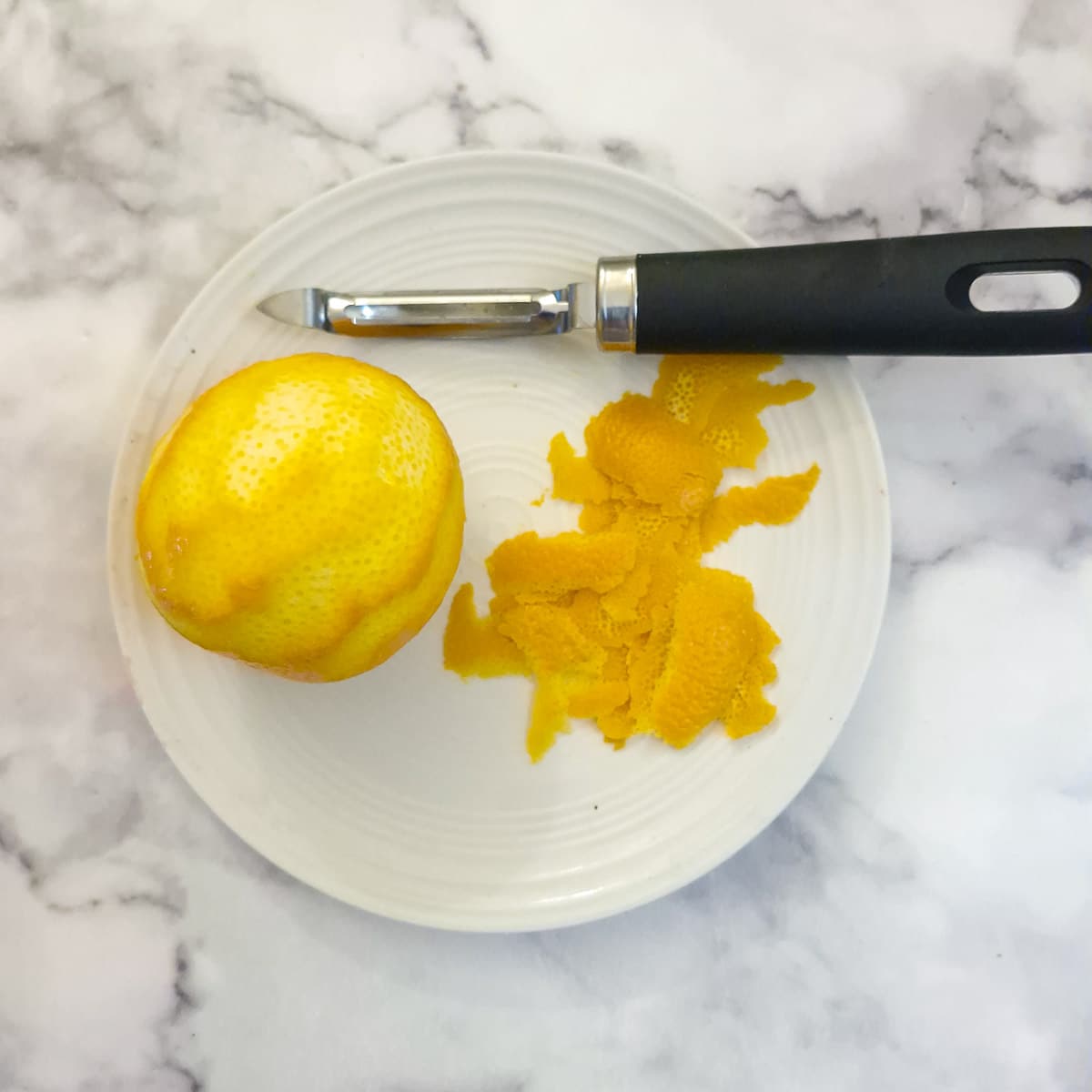 An orange on a plate with the zest that has been sliced off with a vegetable peeler.