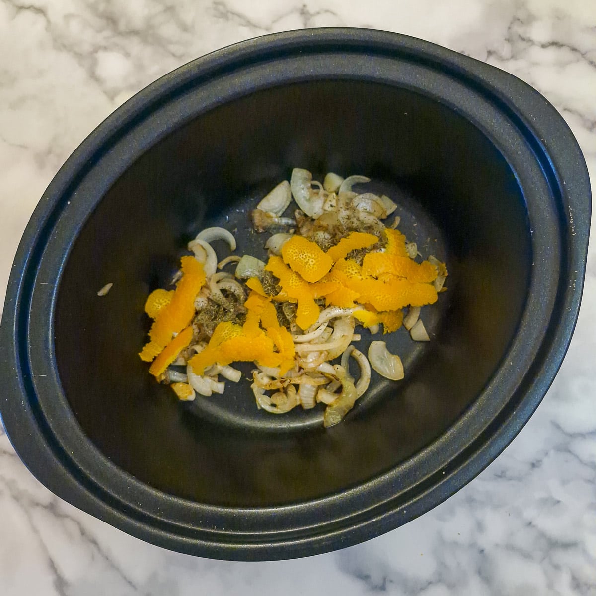 Onions and orange zest in a slow cooker.