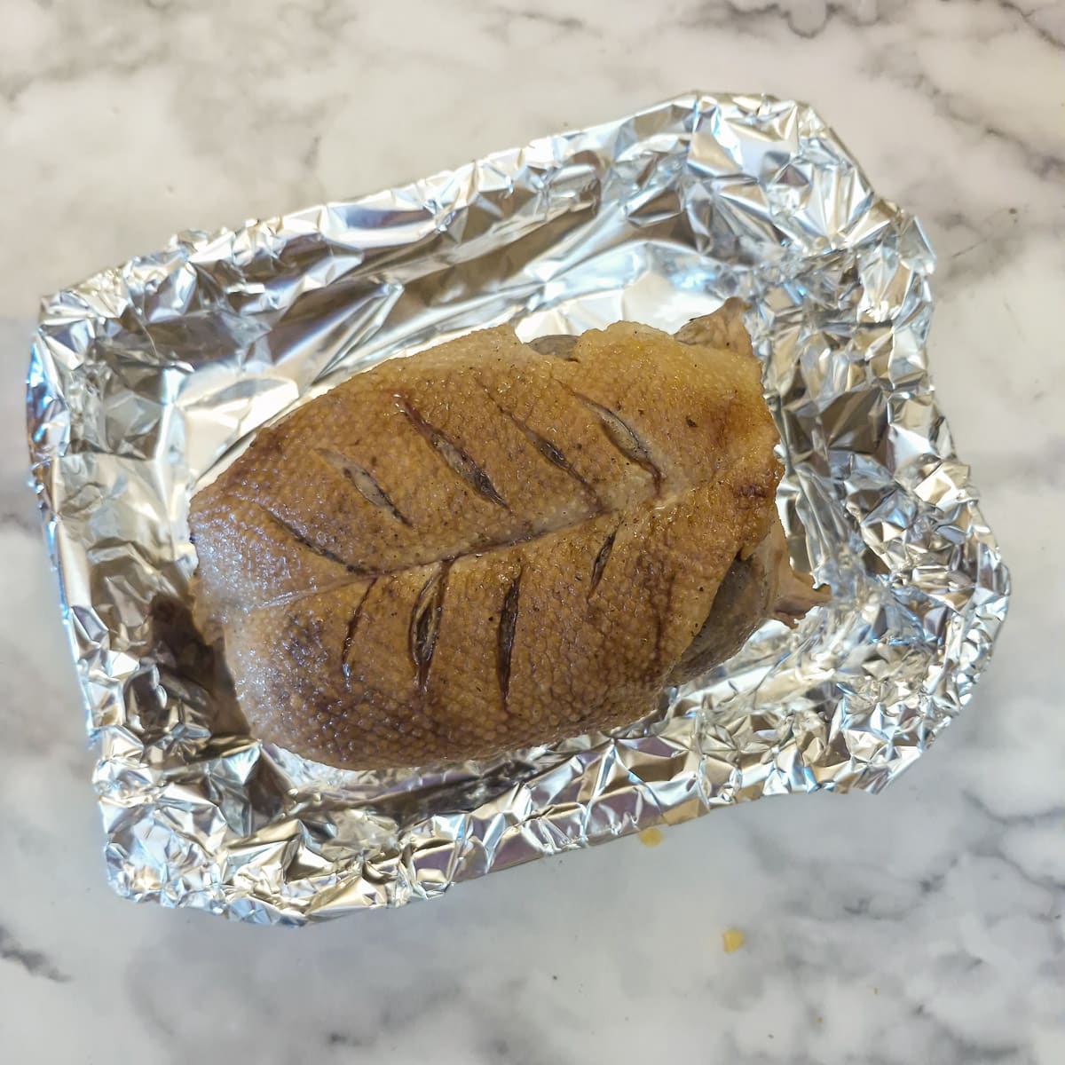 Slow cooked duck crown transferred to a foil-lined roasting pan.