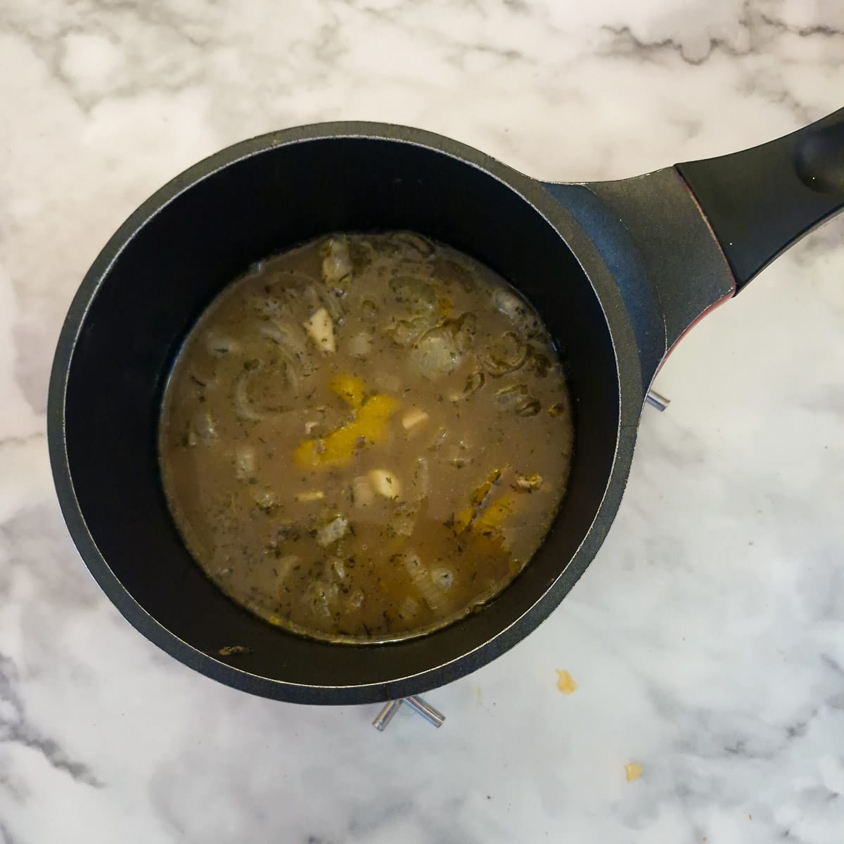 A saucepan containing a cup of cooking liquid, including the onions.