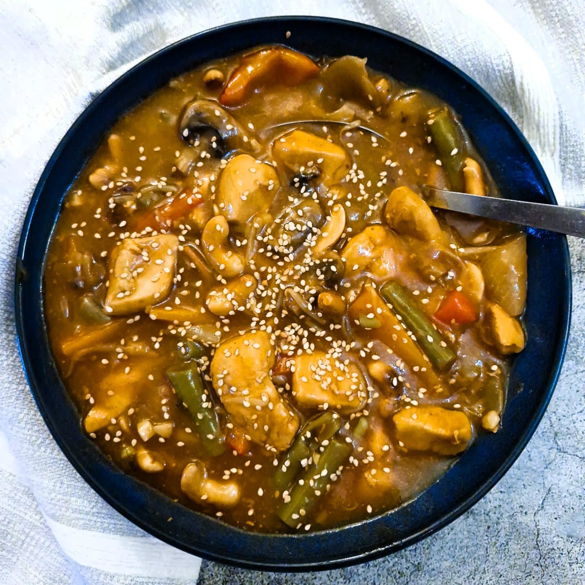 A blue serving bowl containing asian-style garlic chicken with cashews (and lots of sauce).