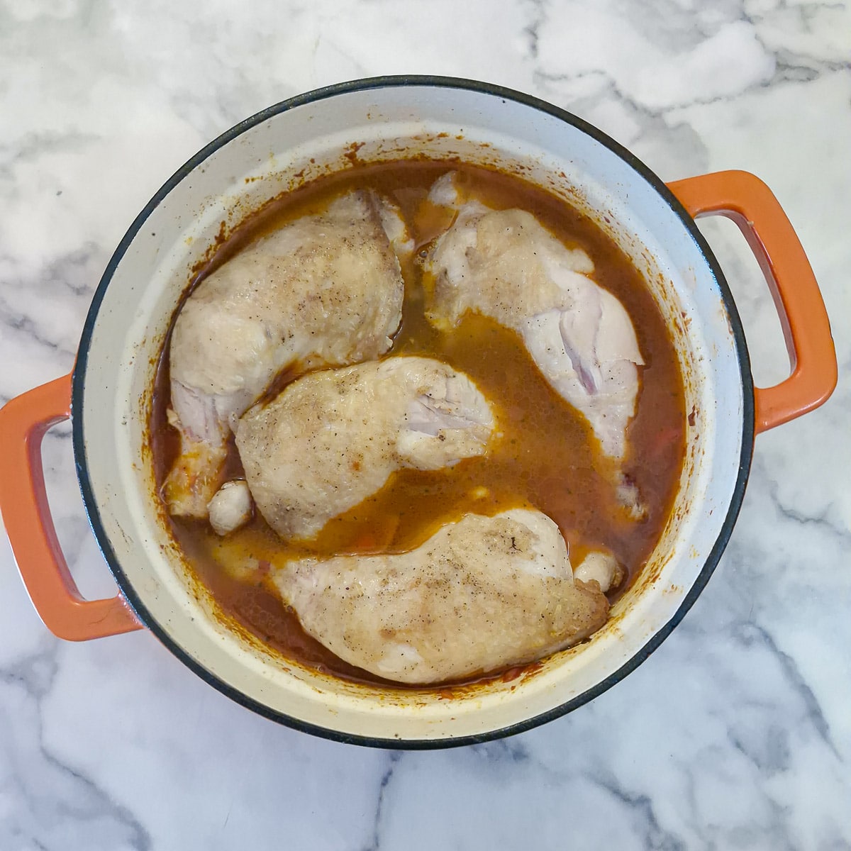 Pieces of chicken in a pan with the paprika-flavoured stock and vegetables.