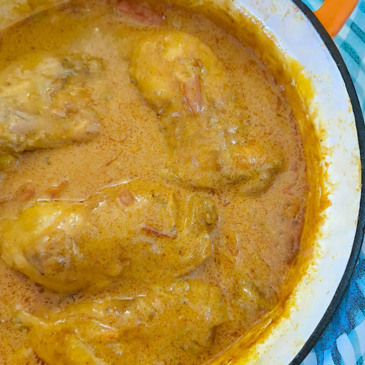 Close up of chicken pieces smothered with paprika sauce in a heavy frying pan.