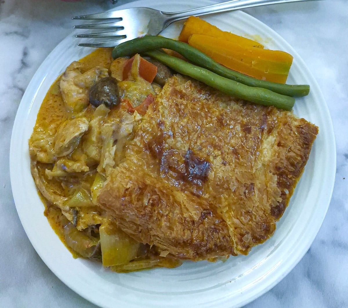 Close up of a slice of paprika chicken pie on a white plate with beans and carrots.