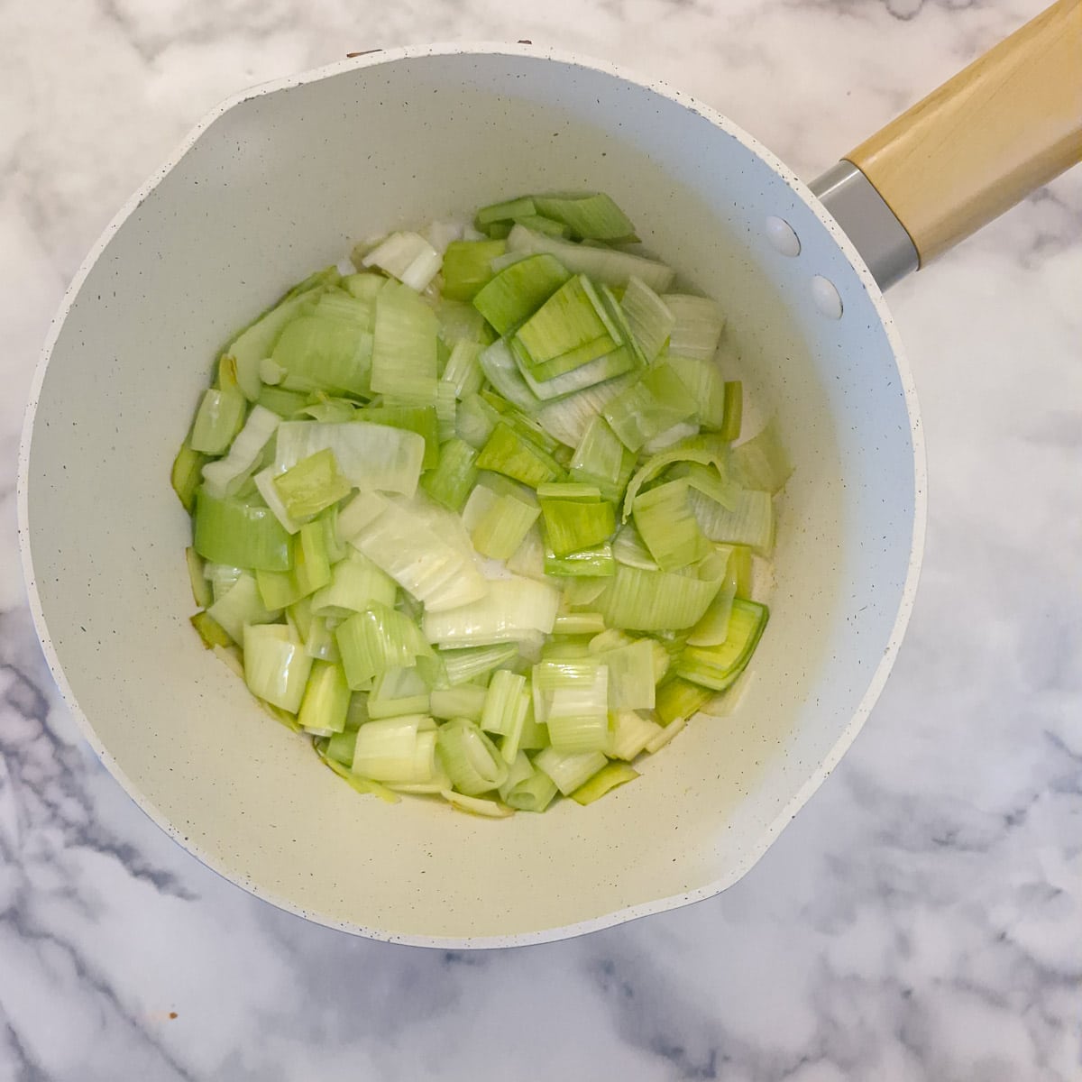 Chopped leeks softening in a saucepan.
