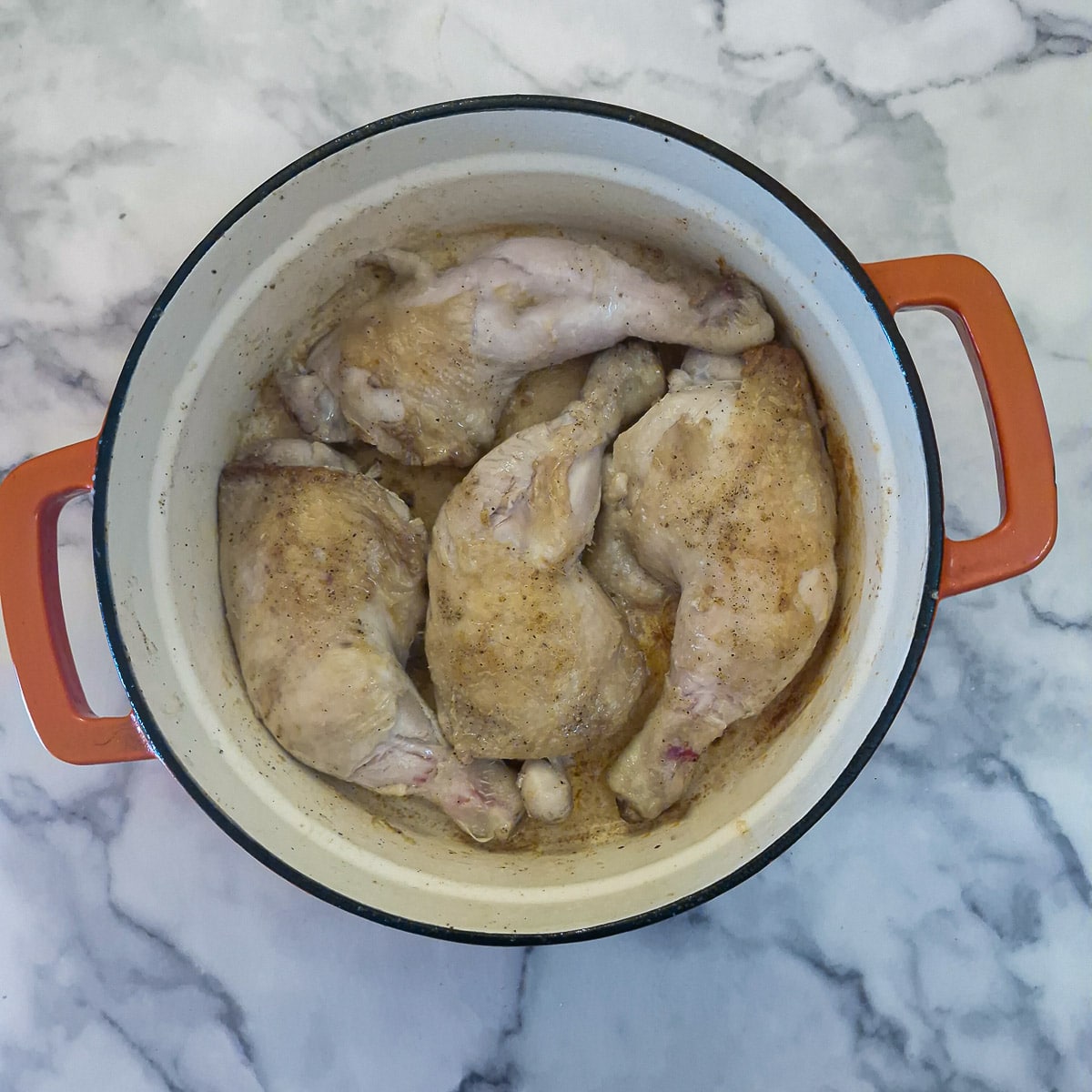 Chicken legs browning in a heavy casserole dish.