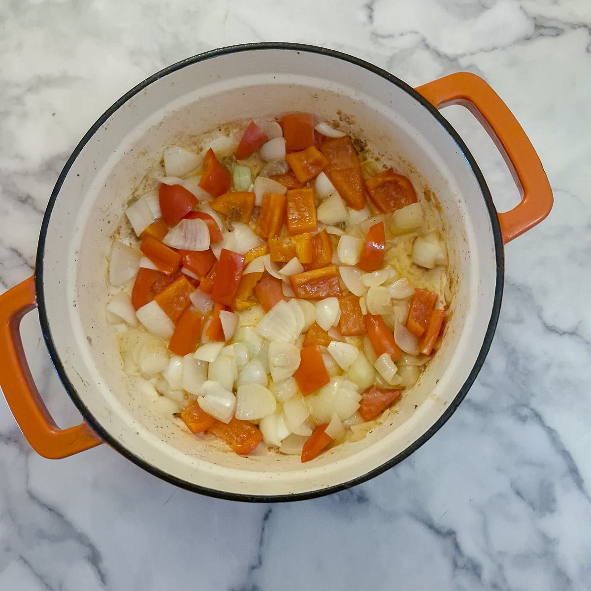 Onions and red bell peppers softening in a pan.