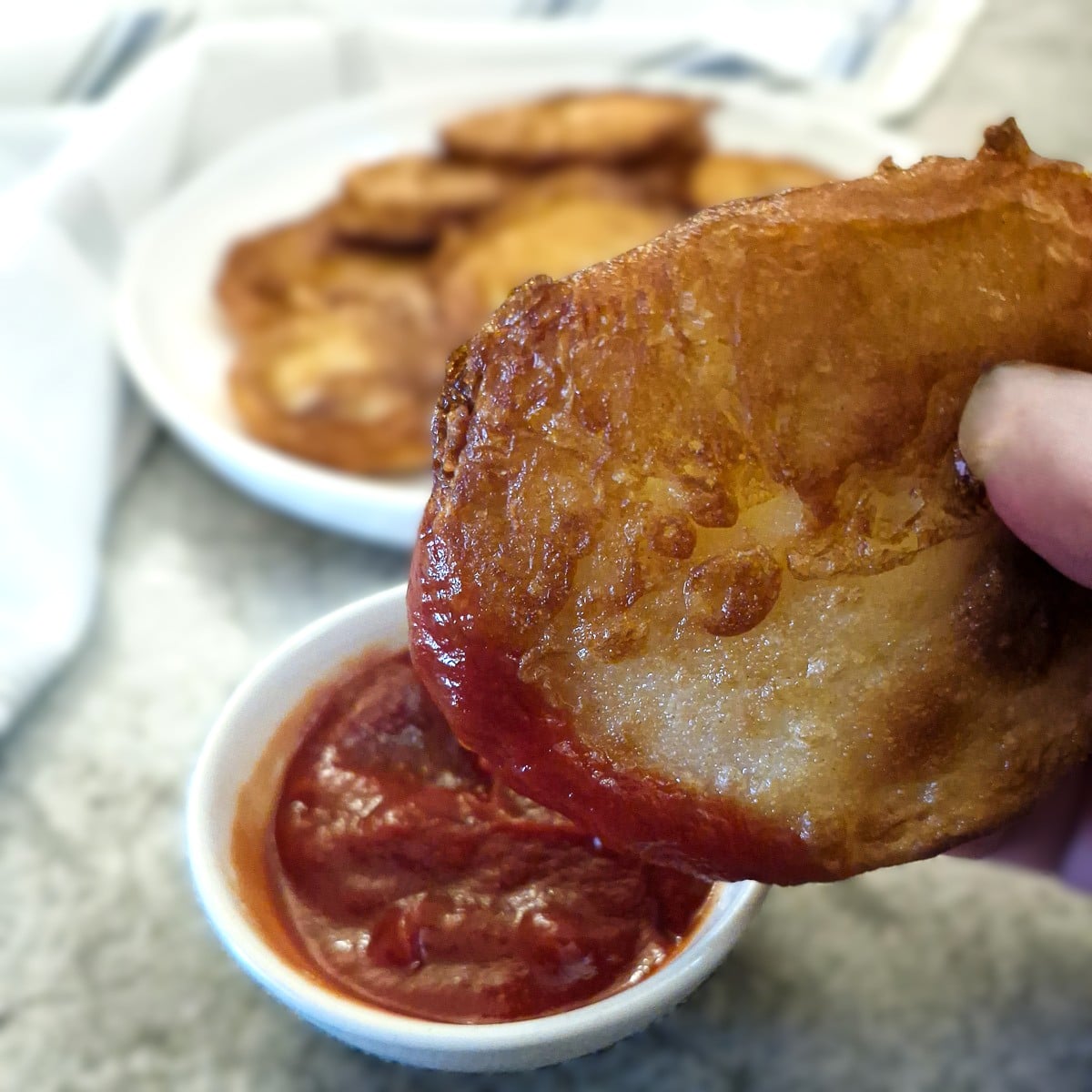 A golden brown scaloped potato being dipped into a bowl of tomato ketchup.