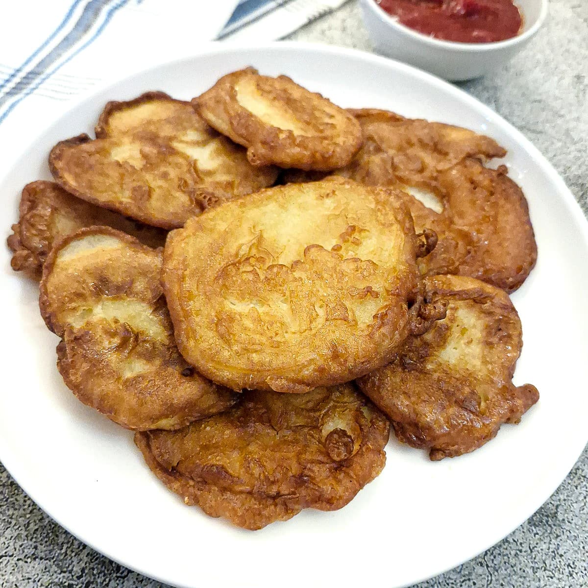 A pile of battered potato scallops on a white plate.