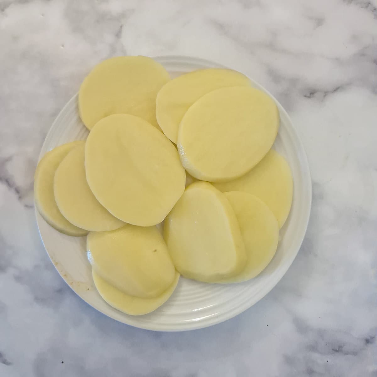 Thinly sliced potatoes on a white plate.