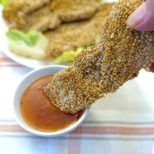 A sesame-coated chicken goujon being dipped into a bowl of dipping sauce.