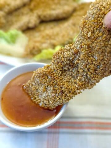 A sesame-coated chicken goujon being dipped into a bowl of dipping sauce.