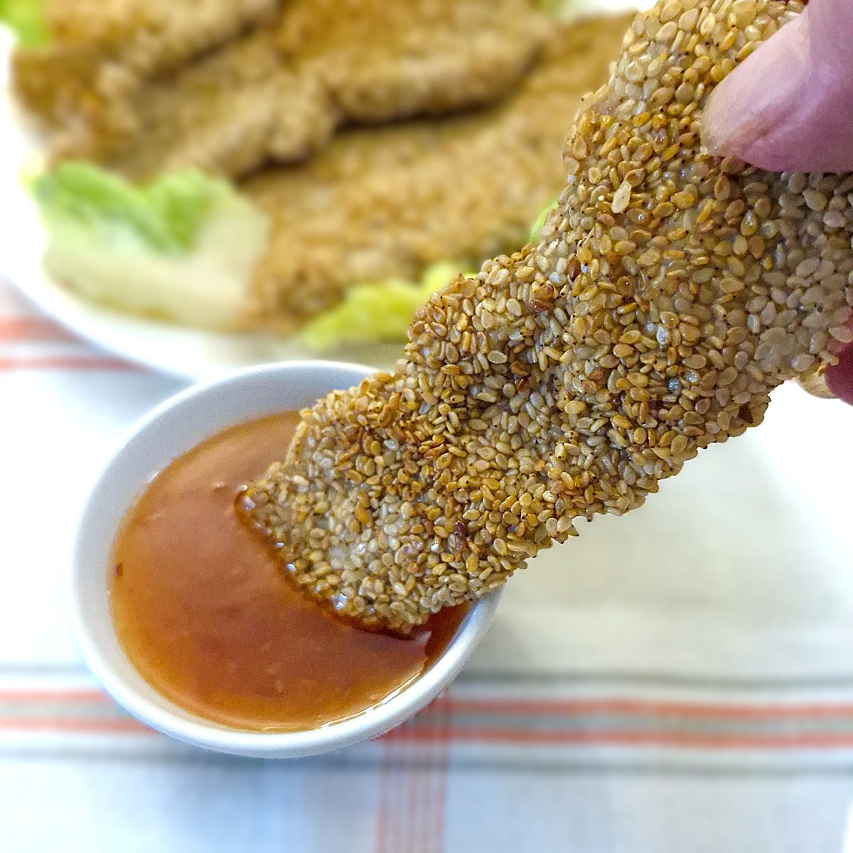 A sesame-coated chicken goujon being dipped into a bowl of dipping sauce.