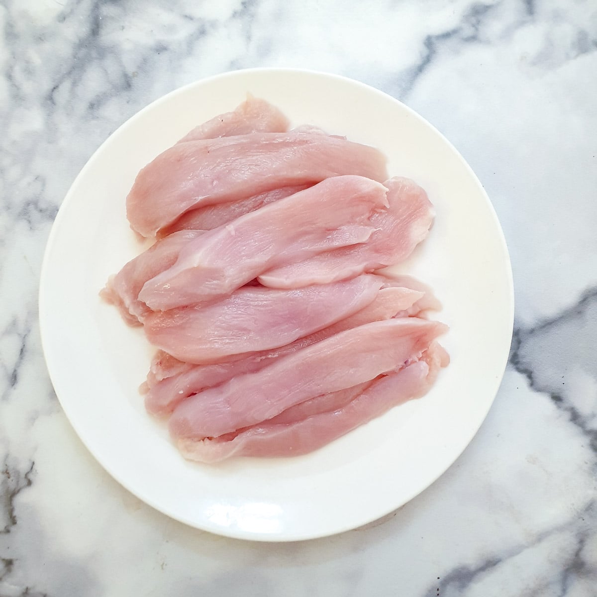 Raw chicken strips on a white plate.