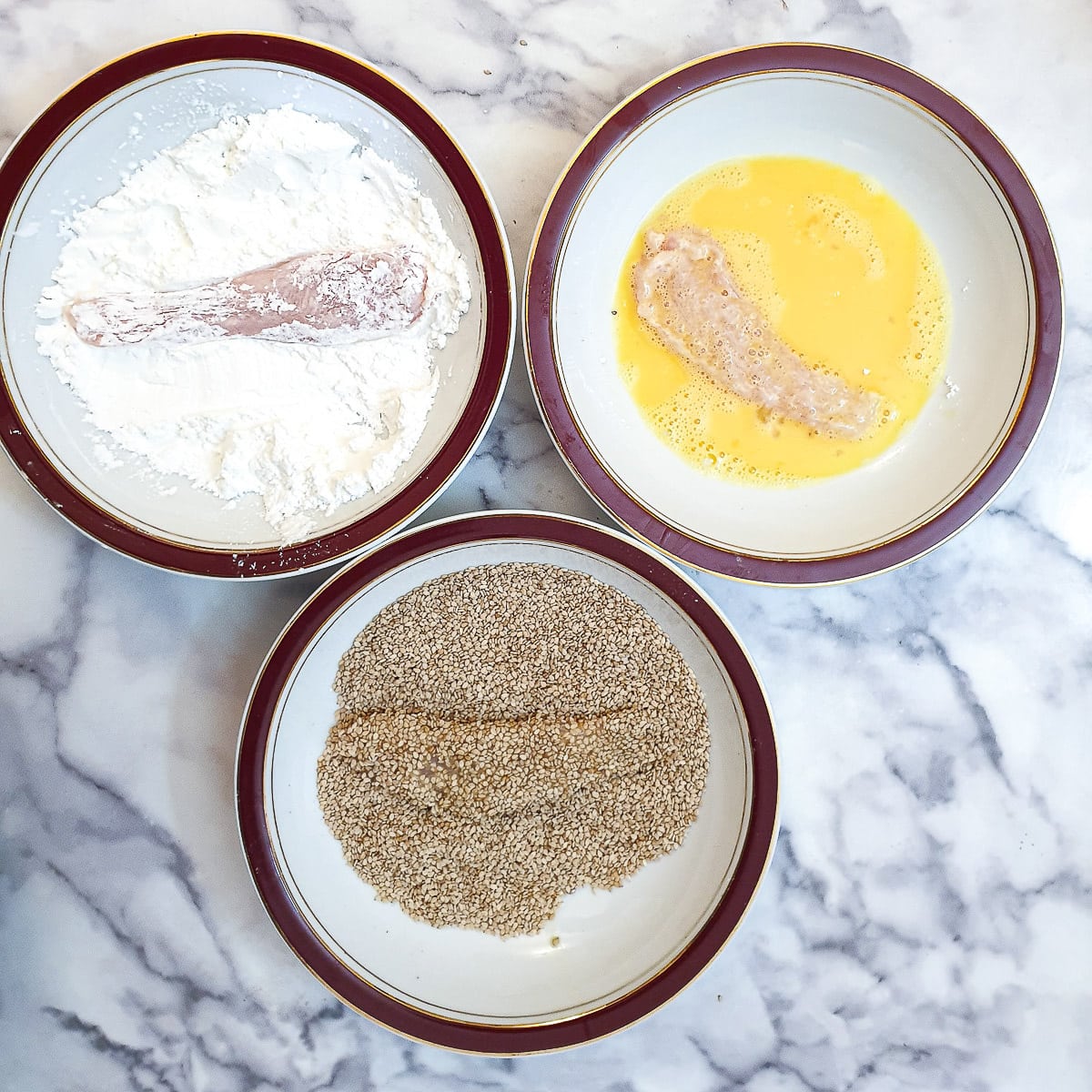Chicken strips being coated in cornflour, beaten egg and sesame seeds.