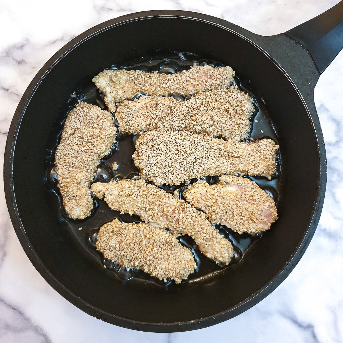 Sesame chicen strips being fried in a frying pan.
