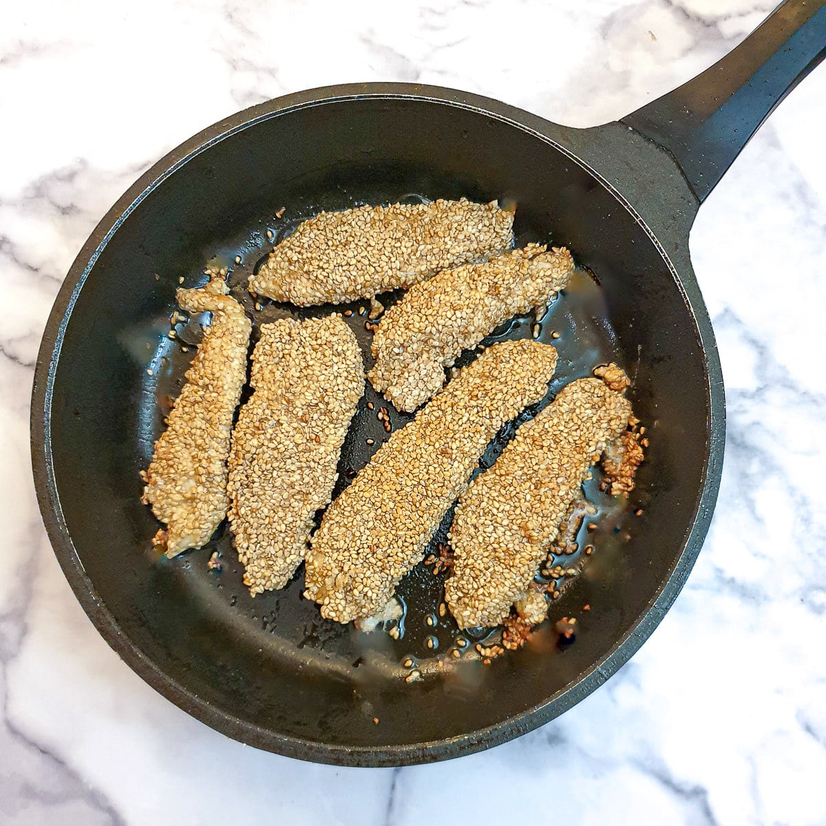 Browned sesame chicken strips in a fryng pan.